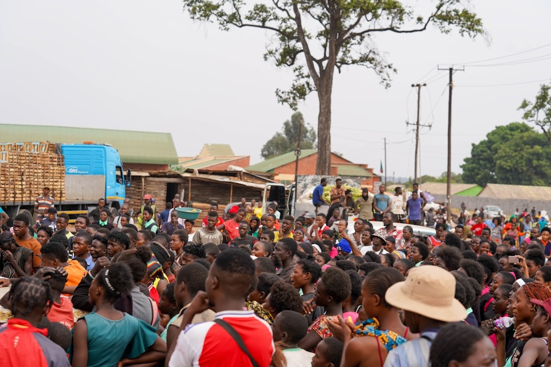 Crowd of people gathered outdoors near buildings and trucks.